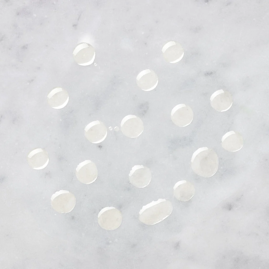 Clear serum drops on white marble, skincare texture for sensitive and uneven skin