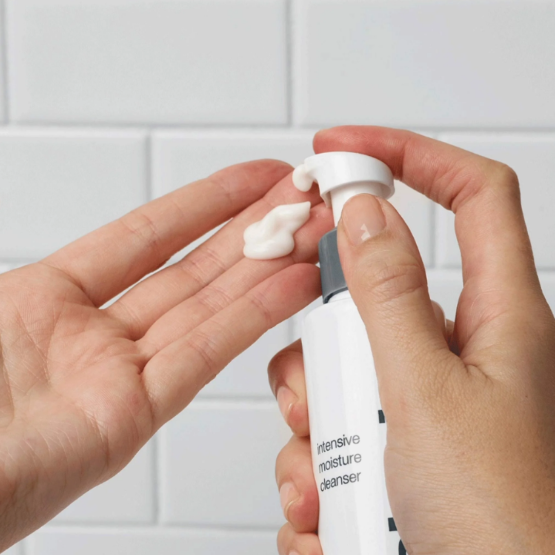 Hand dispensing intensive moisture cleanser foam onto palm against white tile background
