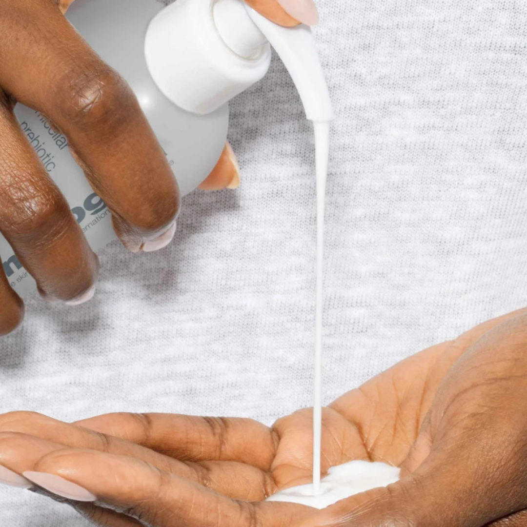 Close-up of person dispensing white micellar prebiotic cleanser into hand on gray fabric background
